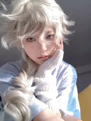 Three-quarter front angle of light gold heat-resistant fiber Lolita wig on model wearing light blue tee and white knit arm cover, hand resting on cheek in contemplative pose