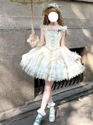 Full front view of light green lolita gown showcasing off-shoulder straps, intricate lace-up front corset closure, and ruffled tulle hemline with delicate lace embellishment, styled with parasol in outdoor garden setting