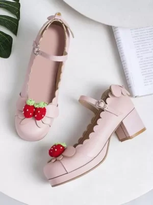 Light pink strawberry platform block heel lolita shoes flatlay overhead view on white table with vintage book and leaf decoration, featuring scalloped trim and dimensional strawberry ornament detail