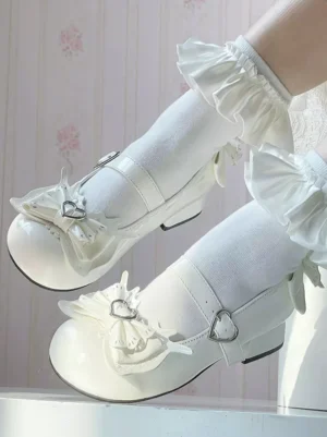 Light sky blue Lolita pumps with heart buckle straps worn on model foot with white ruffled ankle socks, side close-up view showing glossy PU leather and butterfly bow with heart charm detail