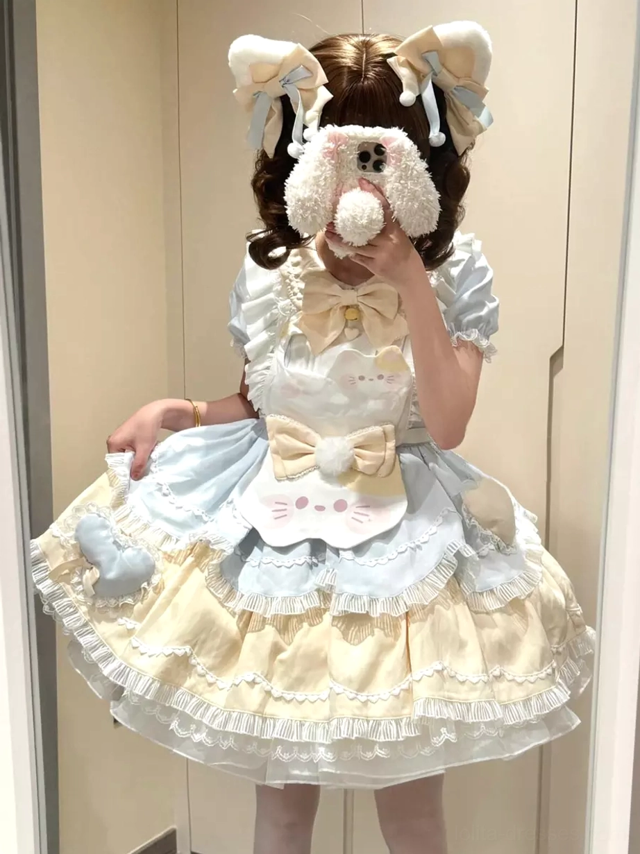 Light sky blue sweet lolita cat dress front mirror perspective featuring beige cat face patch, puffed short sleeves, and ruffled hem on model with flower hair clips marble background