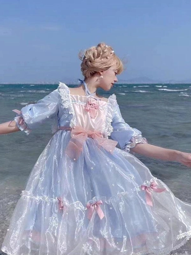 Light sky blue sweet lolita dress full-body side view seaside setting with ruffled collar half sleeves pink bow details