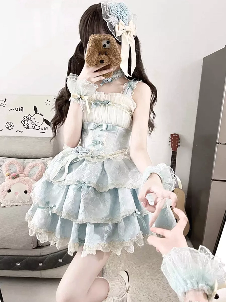 Three-quarter view of sleeveless sky blue lolita dress showing spaghetti straps, lace-trimmed multi-layered skirt, and wrist cuff accessories on sofa backdrop