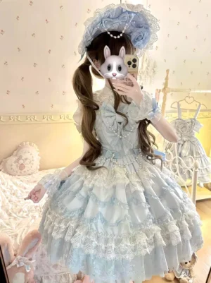 Light sky blue and white sleeveless sweet lolita dress with delicate lace-trimmed ruffled skirt, front chest bow, and full circle skirt design worn by model with twin-tails and blue floral hat - rear-front mirror selfie view