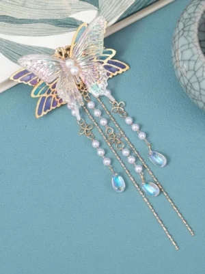 Oblique front view of lilac butterfly hair accessory with dangling pearl and metal chain tassels, featuring the matching core butterfly design against leaf-patterned backdrop and ceramic styling for lolita tea party occasions