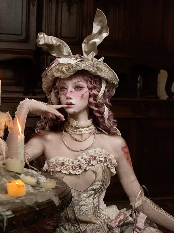 Seated lolita model wearing cream lace arm covers with candle decorations, hand positioning near mouth, delicate lace sleeve detail and vintage aesthetic showcase