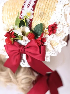 Close-up front view of vintage lolita bonnet showing intricate details: straw hat body, white lace edging, oversized red satin bow, daisy and red berry floral decorations, maroon lace ribbon accent strip
