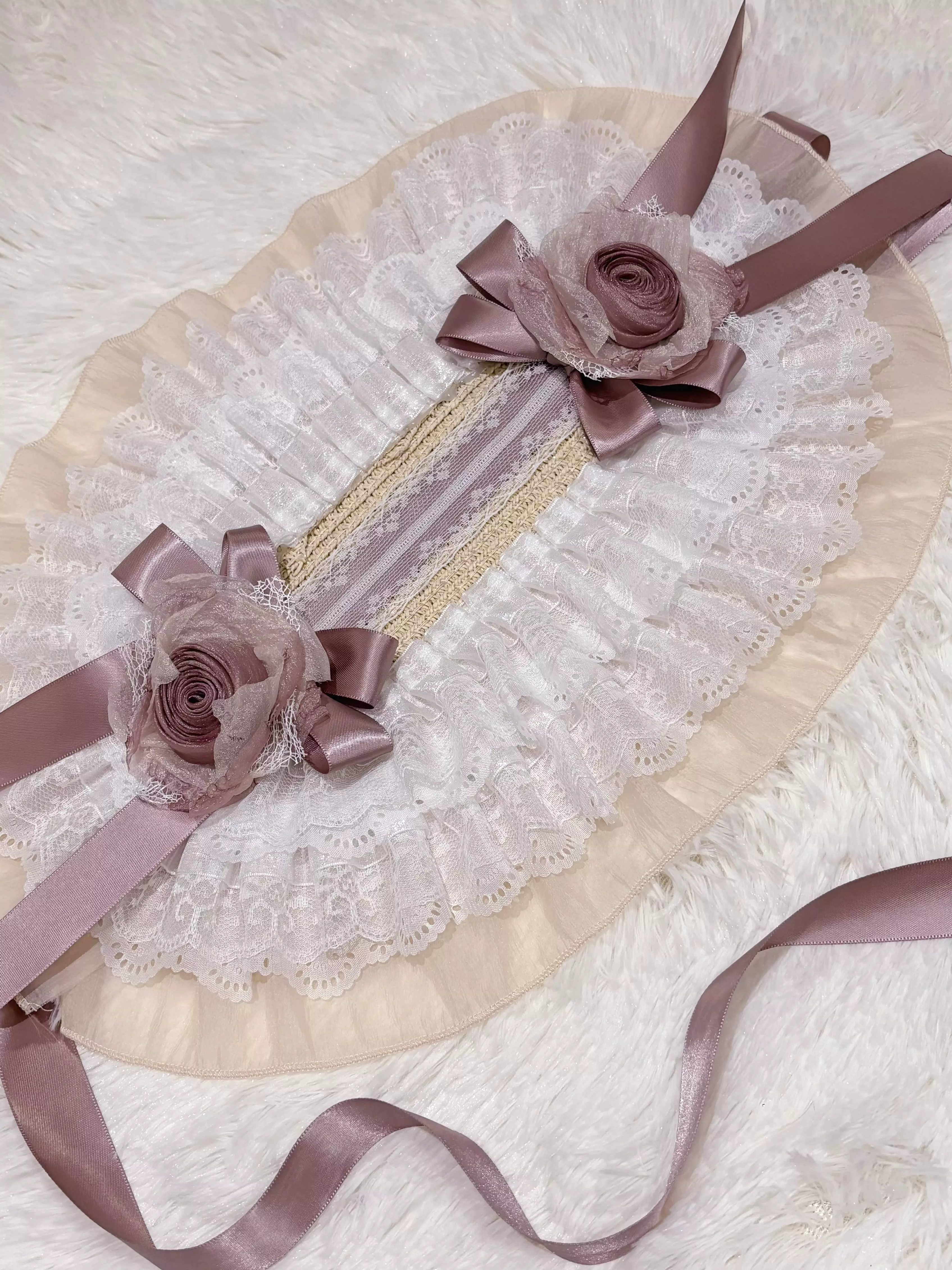 Flat lay product shot of lolita bonnet headdress on fuzzy fabric background displaying two floral bow sets, white lace ruffles, mauve satin ribbons, and overall bonnet construction details