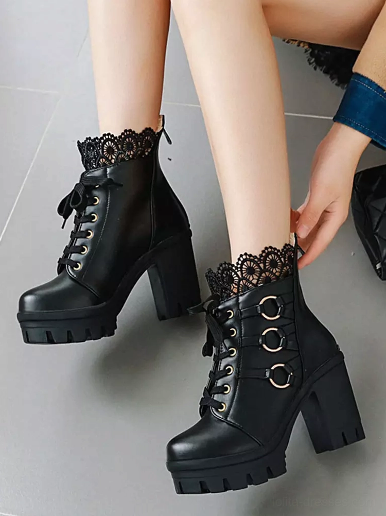 Close-up of black Gothic lolita ankle boots on model hand adjusting boot showing lace trim metal ring accents chunky lug heel details