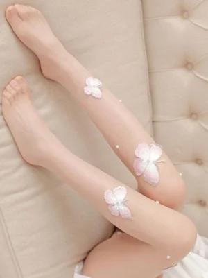 Close-up overhead view of Lolita butterfly embroidered nude stockings with pink and white butterfly embroidery and pearl bead accents on beige tufted sofa