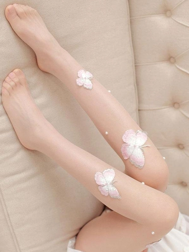 Close-up overhead view of Lolita butterfly embroidered nude stockings with pink and white butterfly embroidery and pearl bead accents on beige tufted sofa