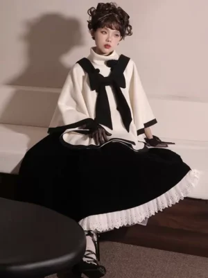 Front seated view of two-tone Lolita winter cape coat with black velvet bow tie detail, paired with black lace Victorian skirt in vintage retro living room setting
