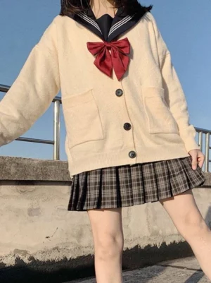 Beige Lolita cardigan sweater with navy sailor collar, full-body front view on rooftop showing red bow, black buttons, and coordinating plaid mini skirt ensemble