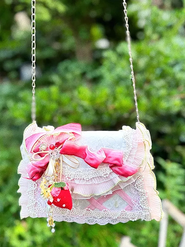 Lolita chain shoulder handbag side front view displaying metal chain strap, strawberry charm, ruffled lace detail, and pink cross webbing with green plant background