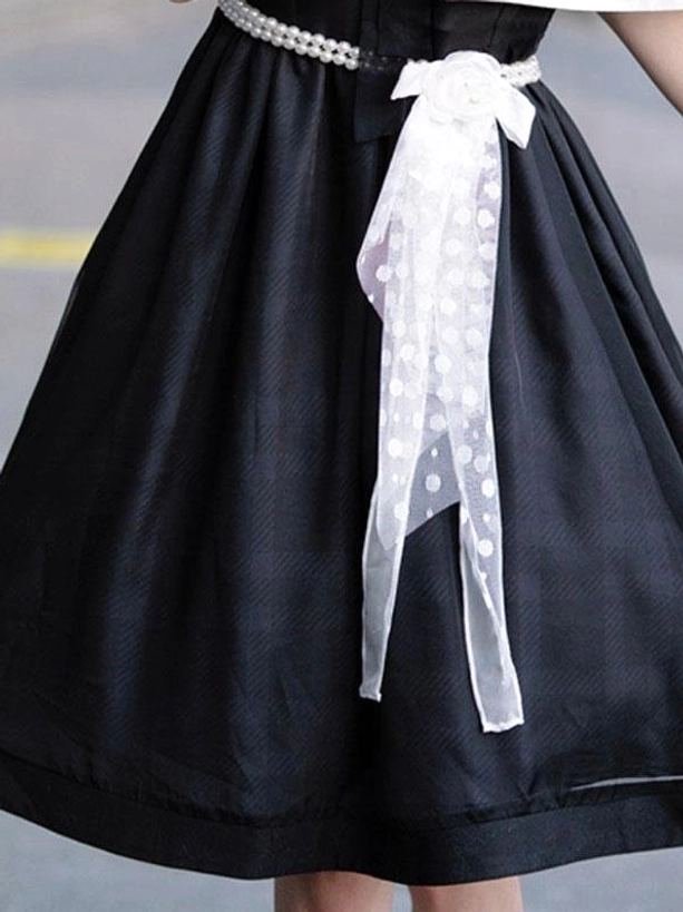 Close-up of lolita dress black fabric with pearl waist belt and polka-dot sheer white bow sash front low angle shot