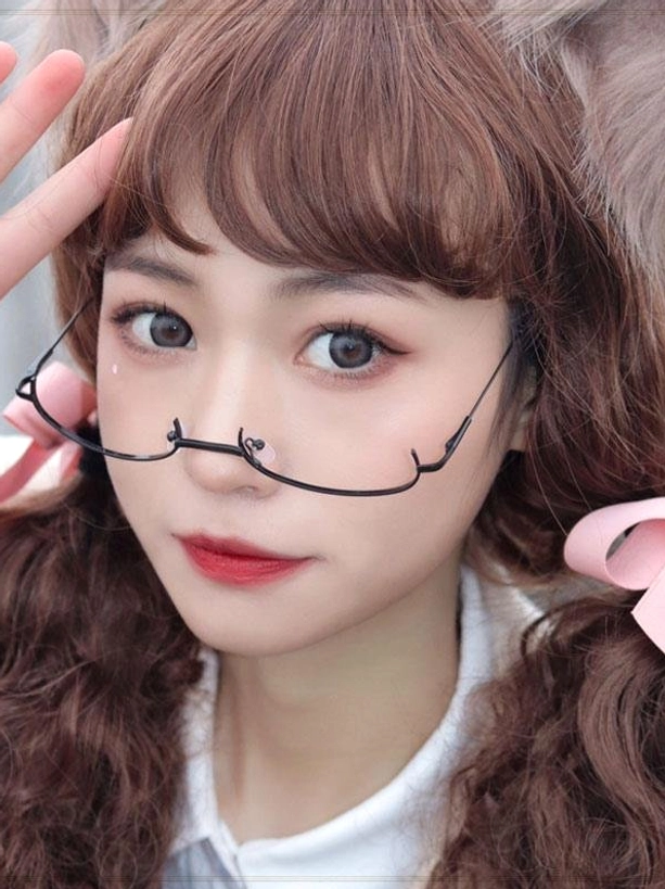 Model styled in lolita aesthetic wearing black half-frame glasses with brown curly wig and pink hair bows, hand touching hair in elegant pose demonstrating glasses chain eyewear coordination