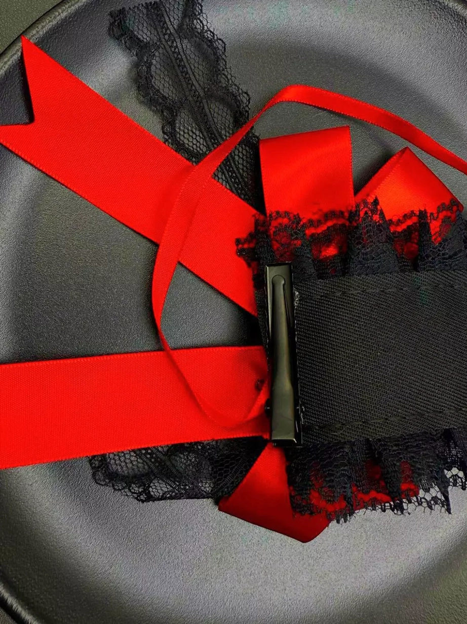 Lolita hair clip accessory photographed from above showing the red satin ribbons, layered black lace, metal hair clip base, and pearl embellishments in detailed close-up