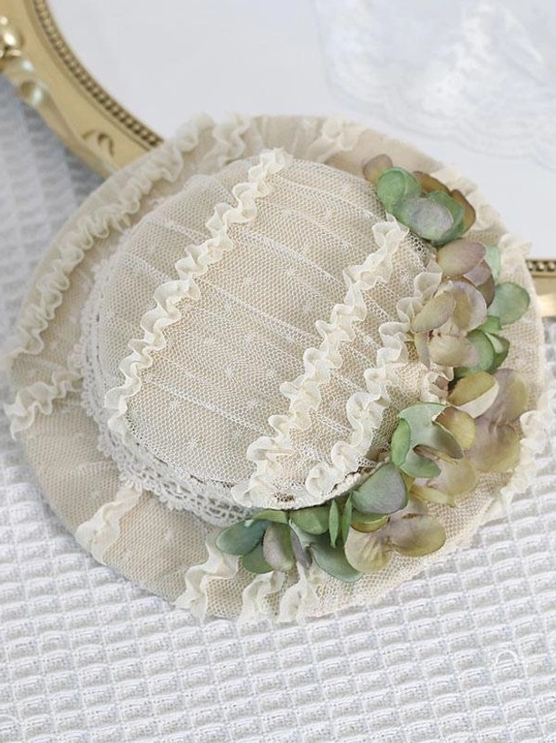 Top-down flat lay of beige dotted mesh Lolita hair clip headdress with green and light brown hydrangea accents and ruffled lace trim