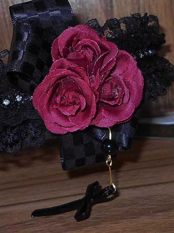 Close-up detail of gothic lolita headband featuring triple wine red rose decorations black ribbon checkered pattern black lace and hanging cross pendant