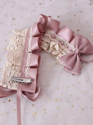 Lolita hair accessory flat lay close-up featuring pink satin ruffles, beige lace trim, and metal hair clip mechanism on starry gold dot background