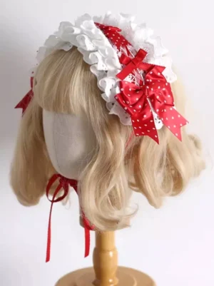 Strawberry-inspired Lolita hair headband with ruffled white lace and red polka-dot bow, front three-quarter angle showing tie strap detail on blonde curly wig