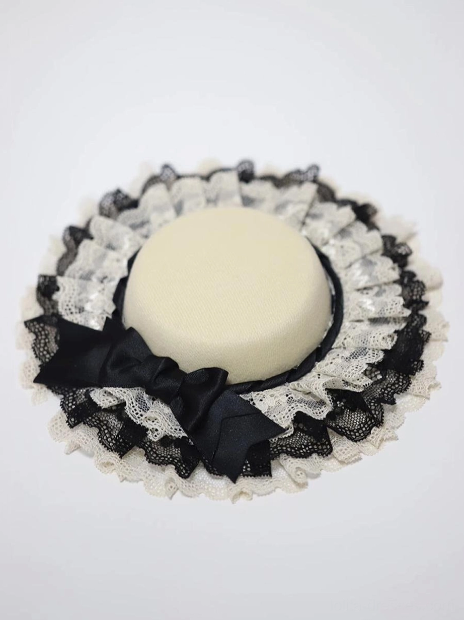 Beige crown Lolita mini top hat overhead flat lay view showcasing dual-tone ruffled lace trim pattern and black satin bow detail from above