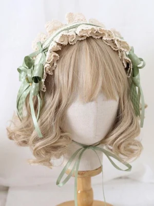 Lolita hair headdress front view displaying dual sage green side bows, cream lace border ruffles, and chin strap ribbon on wooden mannequin head