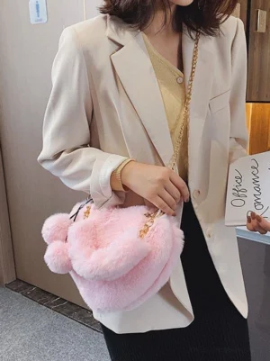 Model wearing pink faux fur heart-shaped Lolita crossbody bag with pom-pom decorations, styled with beige blazer for casual coordination