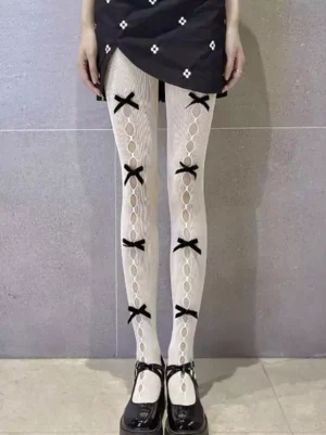 Full front view of model wearing lolita mesh pantyhose with vertical hollow cutout pattern and black bow accents, paired with black Mary Jane shoes, off-white base color, indoor tiled wall background showcasing complete lolita coordinate styling