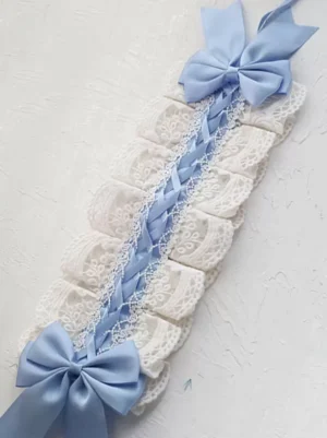 Flat lay top view of Sweet Lolita headdress accessory featuring white embroidered lace, sky blue braided strap, and double satin bows on plain light background, showing construction detail and lace embroidery pattern