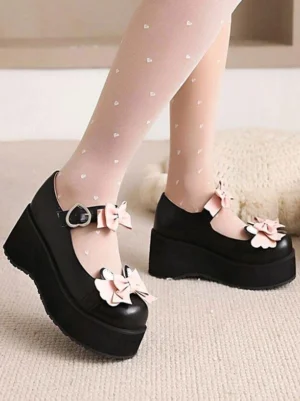 Black Lolita platform shoes side view of feet showing dual pink bows, thick wedge platform sole, and closed round toe with heart-patterned socks on indoor carpet