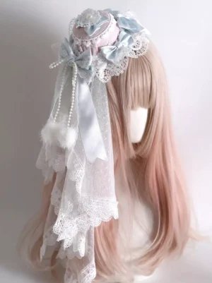 Pastel blue and pink sweet lolita mini hat headdress with attached layered veil, satin bows, pearl tassels and faux fur pom-poms on mannequin with ombre hair, right three-quarter angle showcase