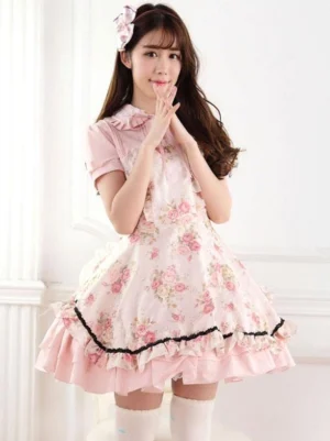 Pink floral lolita dress front three-quarter angle showing model with pink hair bow accessory, cohesive pink color coordination, delicate rose printed skirt section, hands positioned near mouth in sweet pose