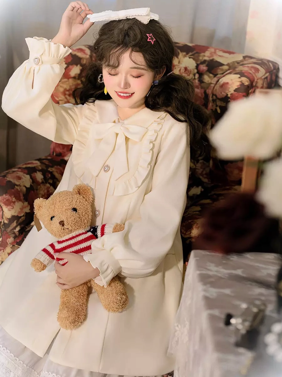 Cream sweet lolita overcoat upper body side view with bishop sleeves ruffled cuffs and a-line silhouette on model on floral sofa