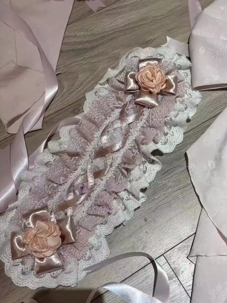Lolita oversleeves with ruffled lace edges, layered ribbons, and 3D pink rose embellishments photographed on wooden surface with draped satin fabrics
