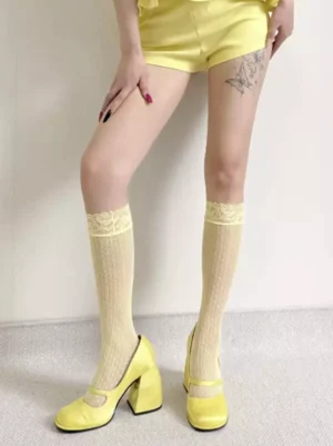 Pale yellow mid-calf lace fishnet socks with ruffled lace cuff and hollow mesh texture, displayed on female model wearing lolita fashion aesthetic, front flat studio view