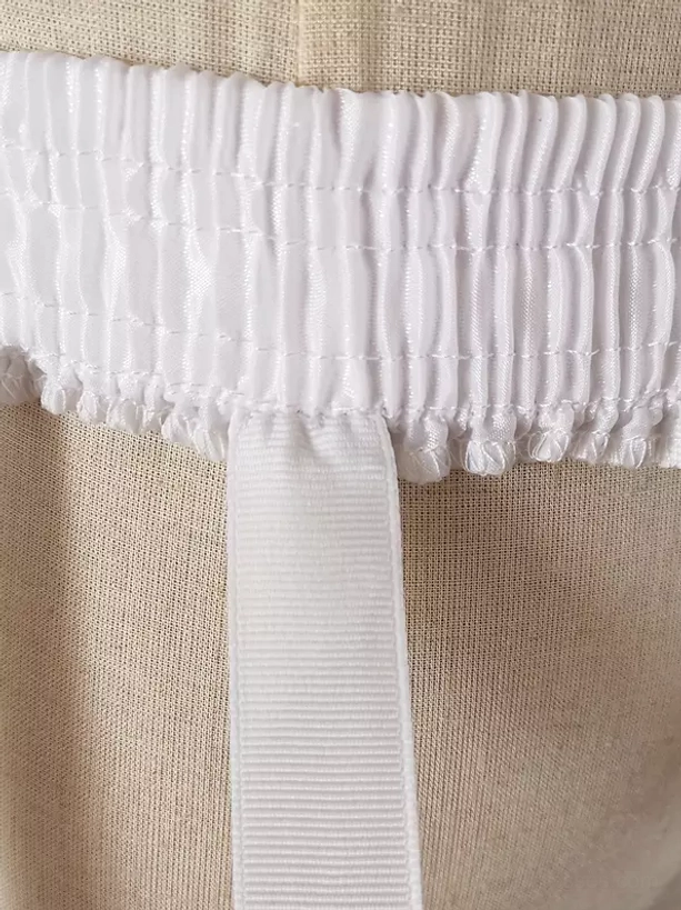 Petticoat waist detail close-up showing shirred elastic waistband and attached woven nylon strap on linen base
