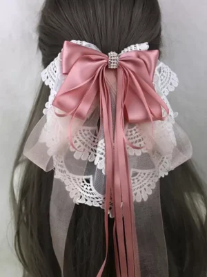 Cute lolita headdress pink satin bow with white lace trim, ribbon tassels, and rhinestone embellishment on dark brown hair mannequin