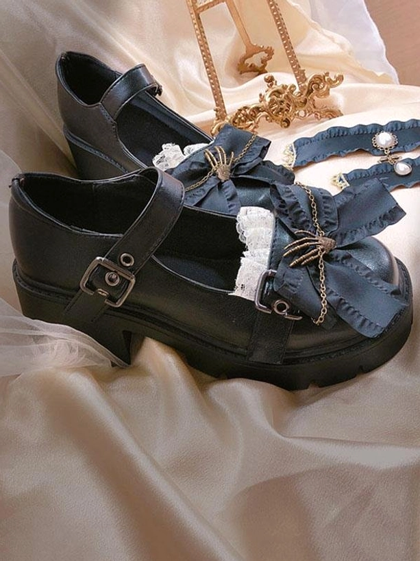 Black Lolita platform shoes side top-down view with skeleton hand bow and chain, lace trim detail, block heel, and buckle strap on golden jewelry background
