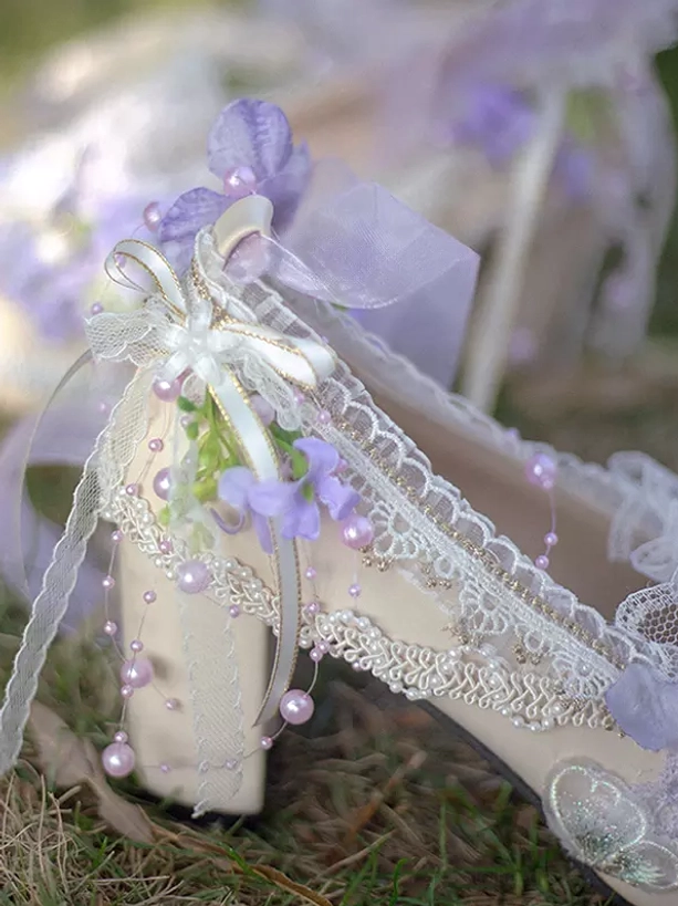 Close-up side view of single Lolita high heel pump featuring purple flowers lace trim pearl string ribbons and stable chunky block heel on grassy ground