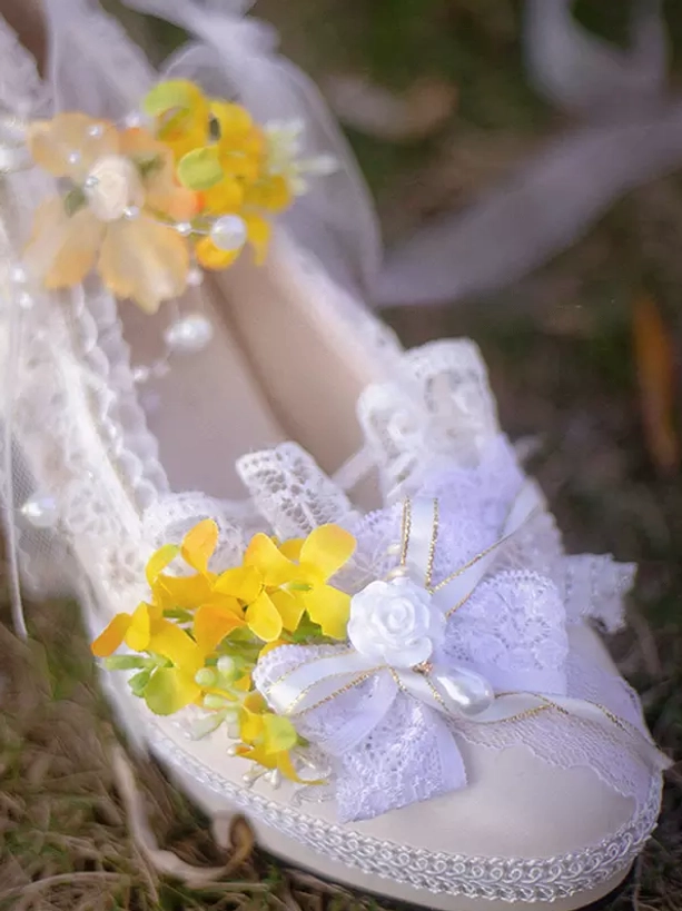 Single Lolita high heel pump with yellow floral accents and delicate lace ribbon bow featuring pearl details shown in close-up top view on grassy ground