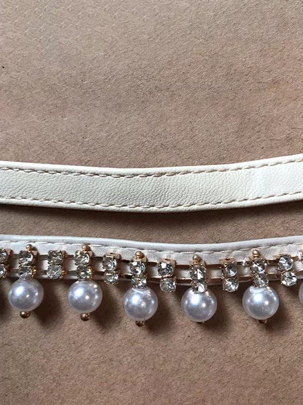 White PU leather ankle strap lolita shoe accessory with rhinestone trim and dangling pearl embellishments, flat lay detail shot showing decorative elements