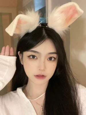 Girl adjusting and positioning cream pink faux fur rabbit ear hair accessory on top of head, medium distance frontal shot showing how Lolita headband sits comfortably on hair with fluffy trim details
