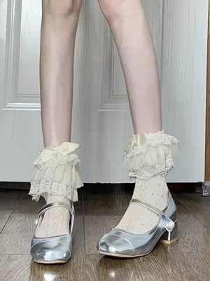 Delicate white lace ruffle socks with cream trim and pearl buckle Mary Jane shoes angled perspective wooden floor