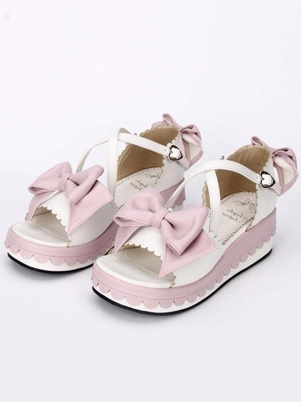 Pink and white lolita platform sandals three-quarter front view showcasing heart-shaped metal ankle buckle and pink bow decorations on white background