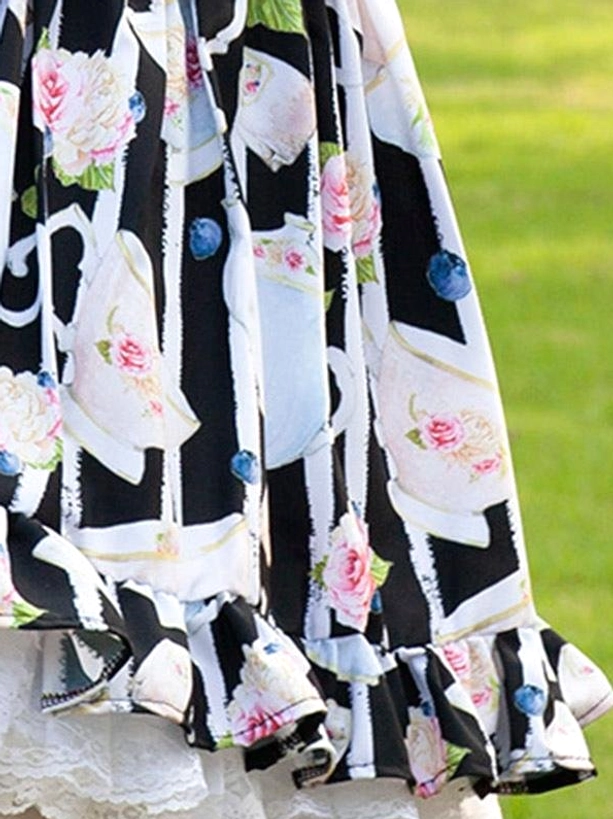 Close-up detail of teacup and rose floral fabric pattern with ruffle lace trim, outdoor grass background