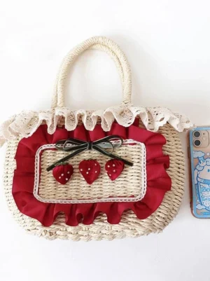 Front flat lay view of lolita tote bag accessory, beige woven straw with white lace trim, black velvet bow, and three red strawberry ornaments with white bead details