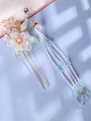 Matching hairpin and tassel earring set coordination featuring gold accents, white resin flower blooms, and blue beaded tassels on light blue desktop – Lolita-inspired Eastern-style accessory pairing