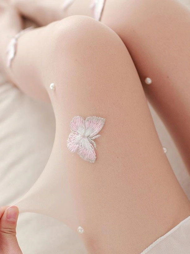 Thigh-high close-up side view of Lolita butterfly stockings showing 3D embroidered pink and white butterflies with pearl details on sheer nude fabric with bedding background