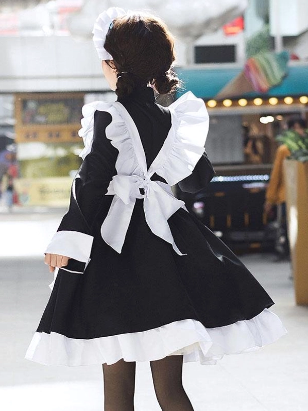 Back view of black maid lolita dress showing large white back bow, ruffled back shoulder straps, and model wearing black sheer stockings